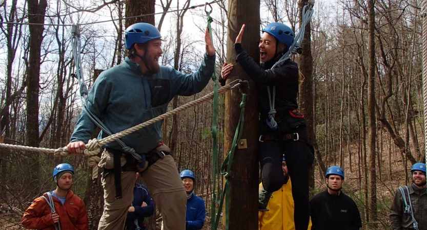 Two people wearing safety gear high five while participating in a ropes course. 